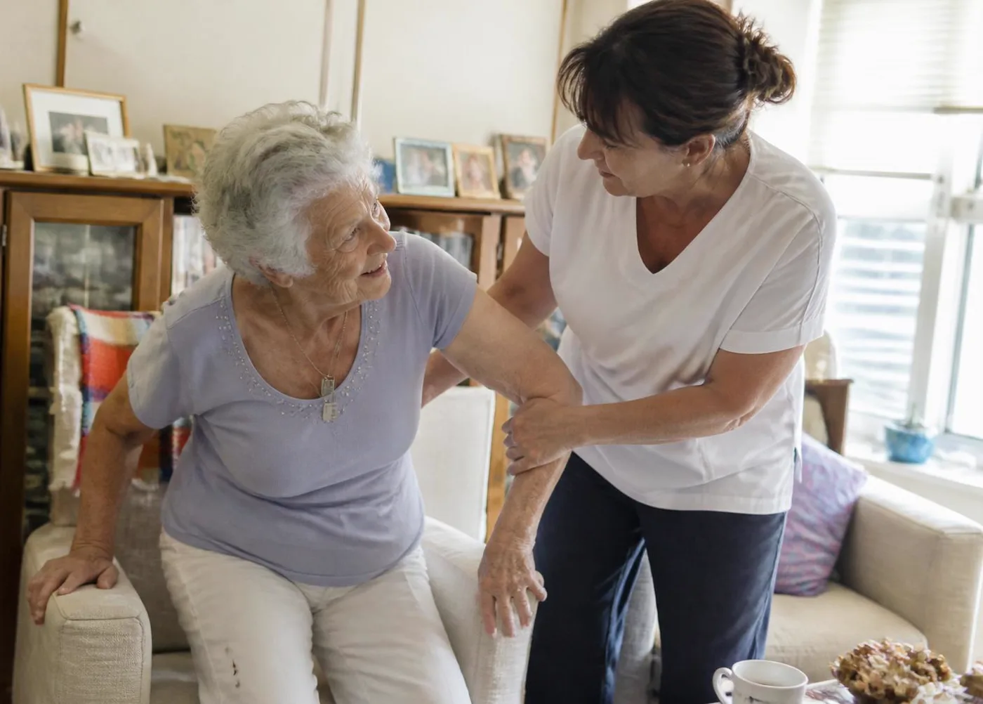 Caregiver steadying a senior client's hand at home with warmth and dignity